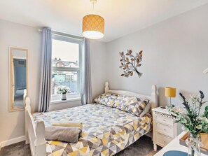 A bedroom with a bed, bedside table, lamp, and a window with curtains. - 3 Bed in Cowes (oc-93982) (Cowes)