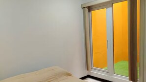Ein Schlafzimmer mit Bett, einem Fenster mit Vorhängen und Blick auf eine grüne Rasenfläche.
