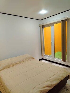 Ein Schlafzimmer mit Bett, einem Fenster mit Vorhängen und Blick auf eine grüne Rasenfläche.