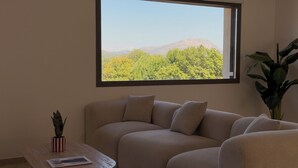 Una sala de estar con un sofá color beige, una mesita, una planta en maceta y una ventana con vistas a la montaña.