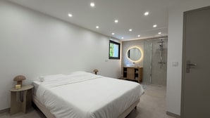 Un dormitorio moderno con una cama grande, mesitas de noche, armario empotrado, baño con ducha y un espejo.
