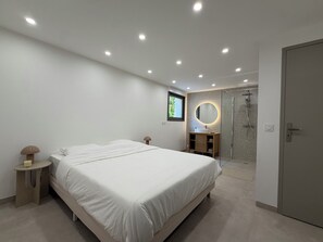 Une chambre moderne avec un grand lit, des tables de chevet, une armoire intégrée, une salle de bain avec douche et un miroir.