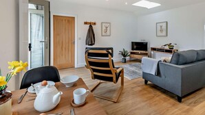 A modern living room with a sofa, a dining table with a chair, a TV stand, and a door. - 4 Bed in Brough (oc-93496) (Brough)