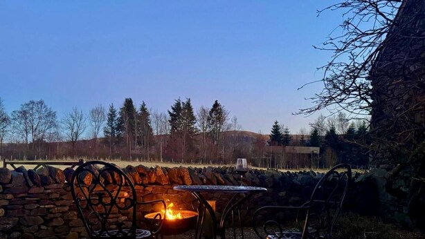 Une terrasse avec un mur en pierre, un foyer et des chaises en métal.