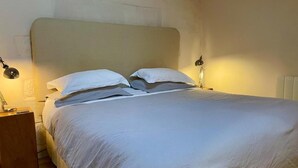 Un lit bien fait, avec du linge de lit blanc, deux lampes de chevet et une table de nuit en bois.
