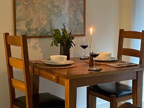 Ein Holztisch ist gedeckt mit weißen Schüsseln, zwei Weingläsern und einer brennenden Kerze.