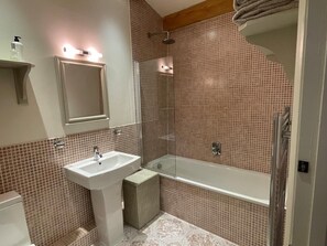 Casa de banho com lavatório branco, espelho e área de duche.