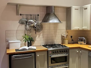 Eine Küche mit Gasherd, Backofen, aufgehängten Töpfen, einem Toaster und einer Topfpflanze.