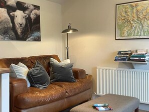 Ein Wohnzimmer mit einem braunen Ledersofa, einer Stehlampe, einer Heizung und einem Bücherregal mit Büchern.