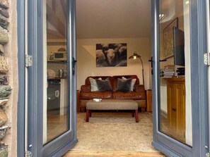 Ein Wohnzimmer mit einem braunen Ledersofa, einer Glastür, die in eine Küche führt, und einem Gemälde an der Wand.