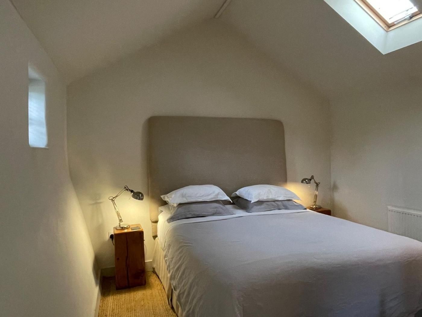 Un dormitorio con una cama individual, dos lámparas de noche, una mesita de madera y un tragaluz.