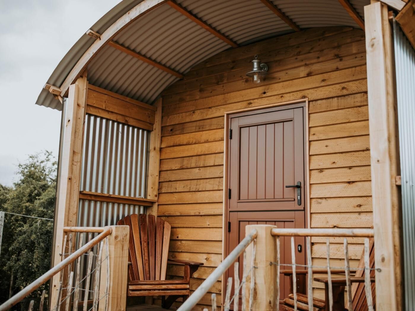 Eine Holzhütte mit einer Metalldür, einer kleinen Veranda mit einem Stuhl und einem Metallgeländer.