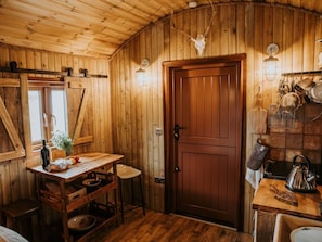 Ein rustikaler Holzraum mit Holztür, einem Tisch mit einer Flasche und einer hängenden Leuchte.