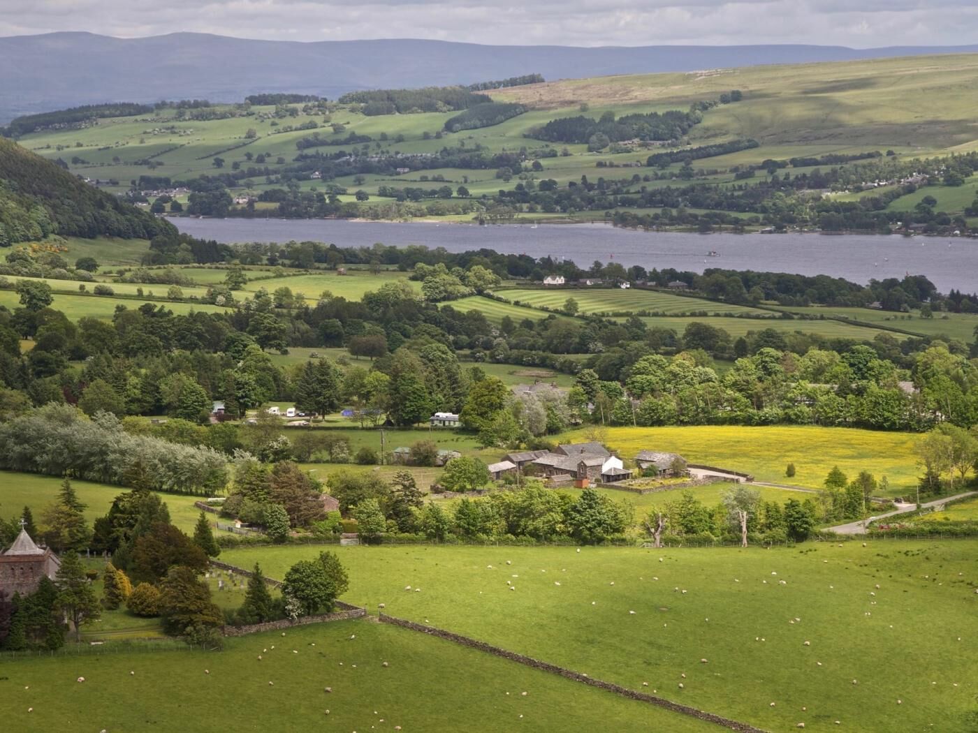 Ländliche Landschaft mit einem See, sanften Hügeln und verstreuten Gebäuden.