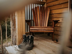 Ein Holzhocker und ein Paar Stiefel auf einer Veranda mit Holzwandverkleidung.