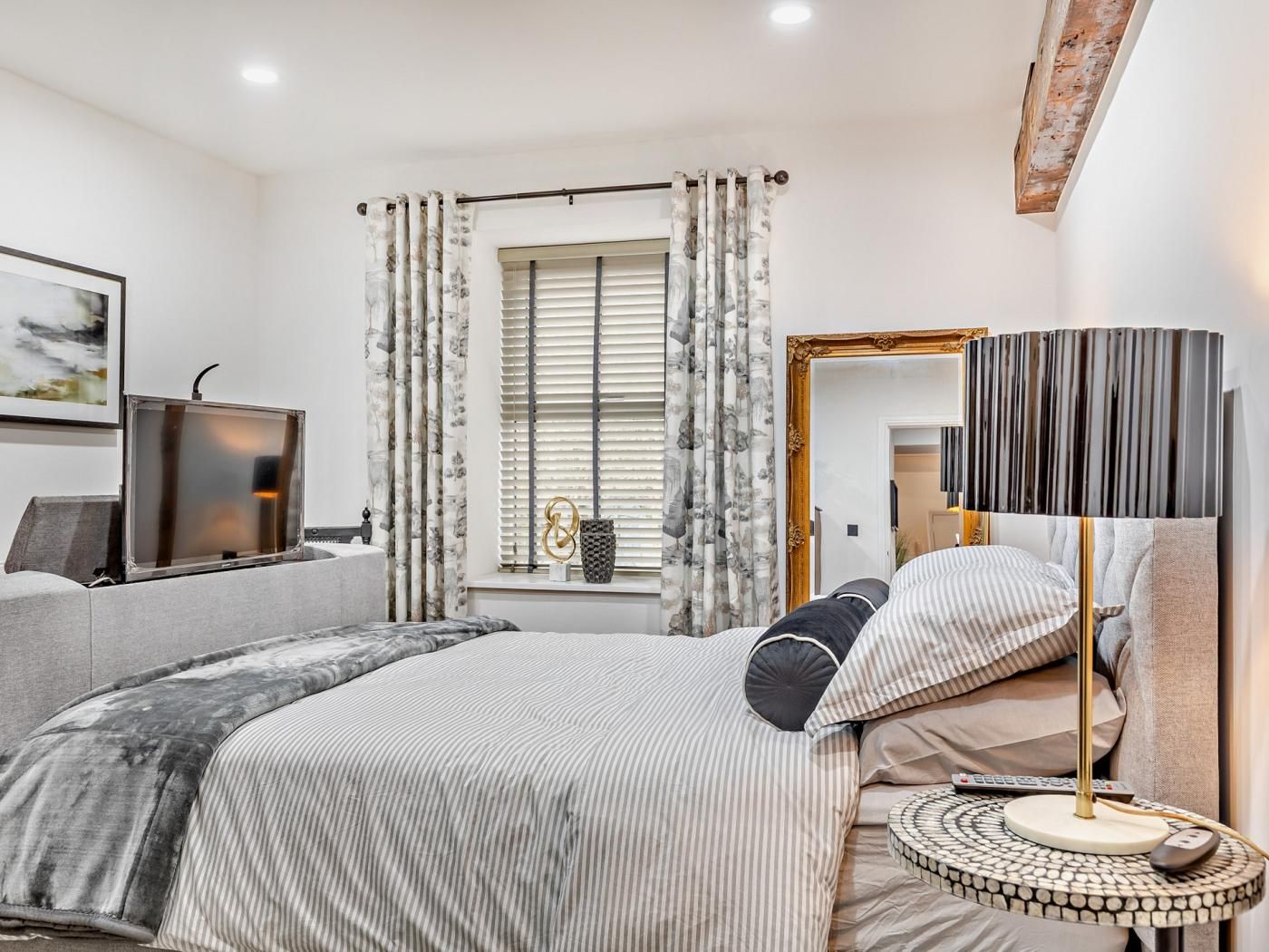 Une chambre à coucher moderne avec un lit, une table de chevet, une lampe et une fenêtre avec des rideaux.