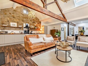 A spacious living room with a leather sofa, a round coffee table, and a stone wall. - 2 Bed in High Peak (oc-94059) (New Mills)