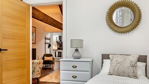 Un dormitorio con cama, cómoda, silla, espejo y una cocina al fondo.