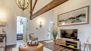 Una sala de estar moderna con un televisor grande, vigas de madera, un otoman redóondo y un cuadro en la pared.