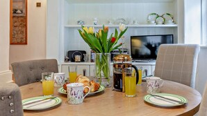 Una mesa de comedor con platos, tazas y una cafetera, rodeada de sillas.