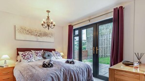 A bedroom with a bed, bedside table, lamp, and a view of the outdoors.
