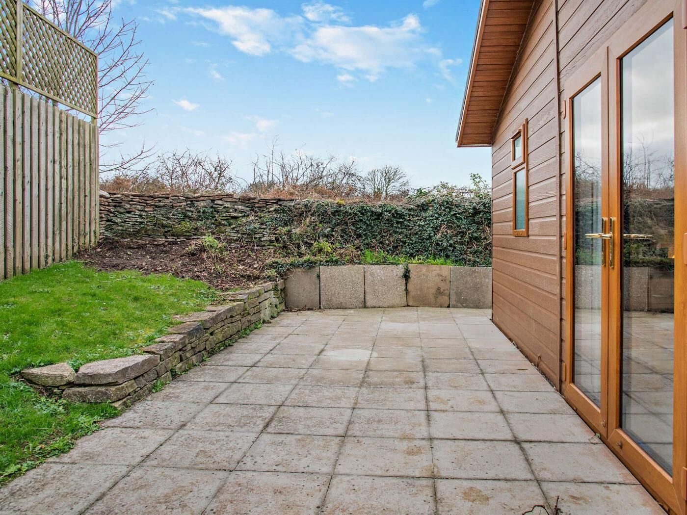 Un patio con pavimento de piedra, cerca de madera y pared de piedra.