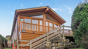 A wooden cabin with a staircase leading to a deck, surrounded by greenery.