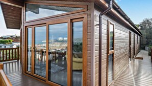A modern house with large glass doors, a wooden deck, and a view of a coastal town.