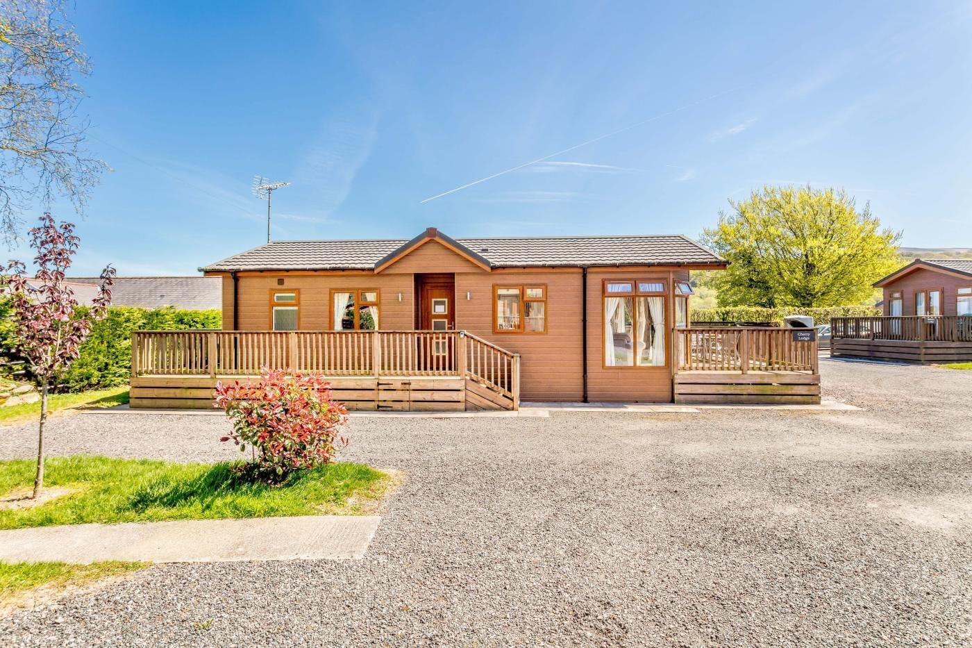 Il s’agit d’un bâtiment de style cabane en bois, doté d’une allée en gravier, d’une terrasse en bois et d’un petit jardin.