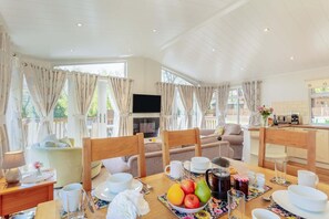 A well-lit living room with a sofa, dining table set for breakfast, and a kitchen area visible through an open door. - 2 Bed in Okehampton (oc-80373) (Okehampton Hamlets)