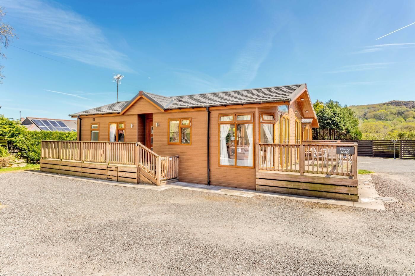Un petit chalet en bois avec un porche, une enseigne indiquant « Cherry Lodge », et une allée gravillonnée.