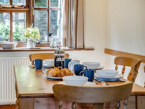 A dining table set with plates, bowls, and blue mugs, with a window view and a radiator below. - 2 Bed in Hereford (oc-94018) (Dorstone)