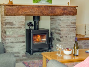 A cozy room with a stone fireplace, a modern wood-burning stove, and a dining table with wine glasses and a bowl of snacks. - 2 Bed in Hereford (oc-94018) (Dorstone)