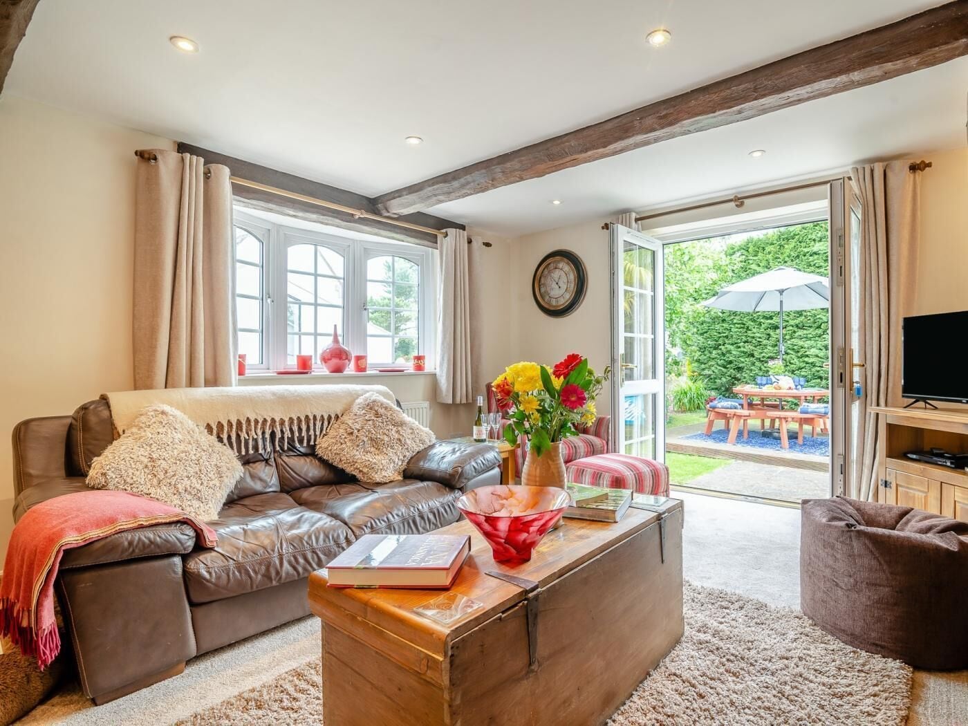 Ein Wohnzimmer mit Ledersofa, Couchtisch aus Holz und Blick auf den Garten durch die offene Tür.