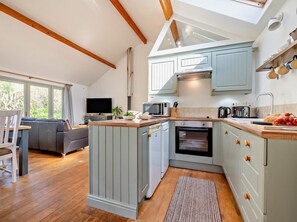 A modern kitchen with a built-in oven, microwave, and sink, a dining area with a sofa, and a TV. - 2 Bed in St. Ives (oc-rgton) (Carbis Bay)