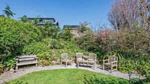 Ein Garten mit Sitzgelegenheit, einer Rasenfläche und einem Gebäude im Hintergrund.