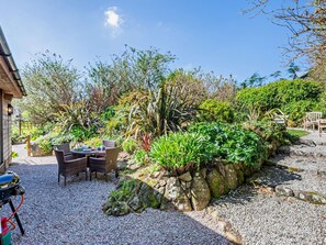 A patio area with a table and chairs, surrounded by a variety of plants and a stone wall. - 2 Bed in St. Ives (oc-rgton) (Carbis Bay)
