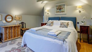 Een slaapkamer met een groot bed, twee nachtkastjes, een kaptafel, een stoel en een schilderij aan de muur.
