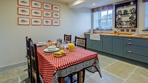 Een eethoek met een rood-wit geruit tafelkleed, een keuken met blauwe kastjes, en wanddecoratie bestaande uit afbeeldingen van vissen.