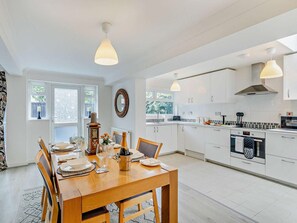 Een moderne keuken met witte kasten, een eethoek met een houten tafel en hanglampen.