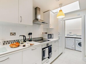 A modern kitchen with a microwave, oven, and a sink. There is a window above the sink and a washing machine in the adjacent room. - 2 Bed in Stratford -upon- Avon (oc-41540) (Stratford-upon-Avon)