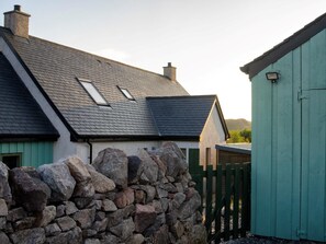 Eine Steinsäule, ein Haus mit schrägem Dach und ein grünes Gebäude.