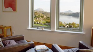 Una habitación con vista a un lago y montañas, un sofá, una mesa con un libro y un cuadro en la pared.