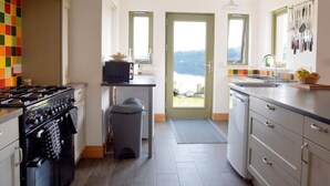 Una cocina con estufa, microondas y lavabo, un cubo de basura y vista a un lago a través de una puerta.