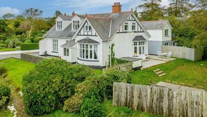 Une maison à deux étages, avec une façade blanche, de nombreuses fenêtres et une cour arrière clôturée.