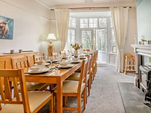 A dining room with a long wooden table set for a meal, a fireplace, and a view through large windows. - 6 Bed in Aberaeron (oc-74151) (Ffos-y-ffin)