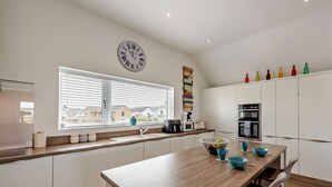 Eine moderne Küche mit einer zentralen Kochinsel, weißen Schränken, einer Wanduhr und einem Fenster mit Jalousien.
