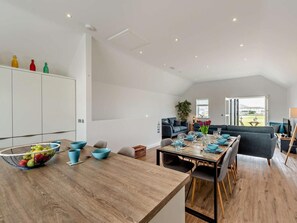 Et moderne spiseområde med et træbord dækket til fire personer, en grå sofa og udsigt til det fri.