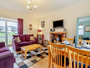 Ein Wohnzimmer mit Sofa, Couchtisch, Kamin, Fernseher und einem Essbereich mit Stühlen und Tisch.