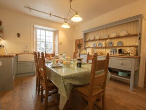 A dining area with a table set for four, wooden chairs, a kitchen area with a microwave and shelves with dishes. - 3 Bed in Penrith (oc-74159) (Shap)